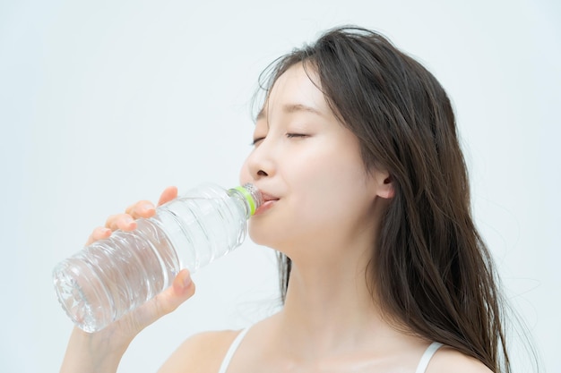 Женщина пьет воду из пластиковой бутылки в помещении