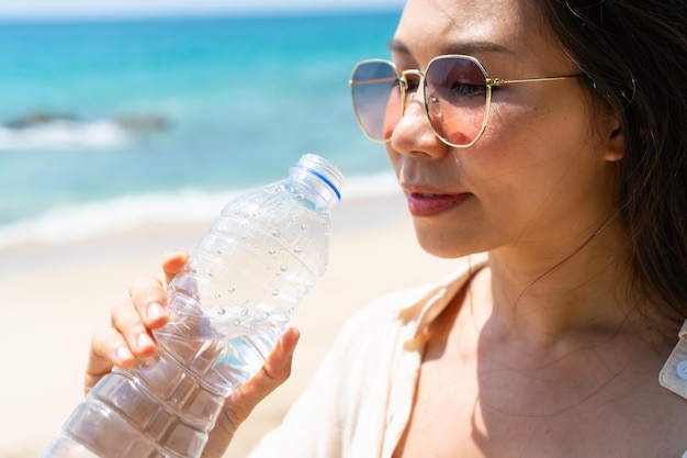 Woman drinking water from plastic bottle in summer sunlight by\
the sea concept of health and freshness thirst water purification\
closeup copy space