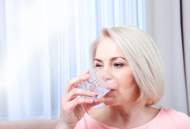 自宅のソファに座って水を飲む女性