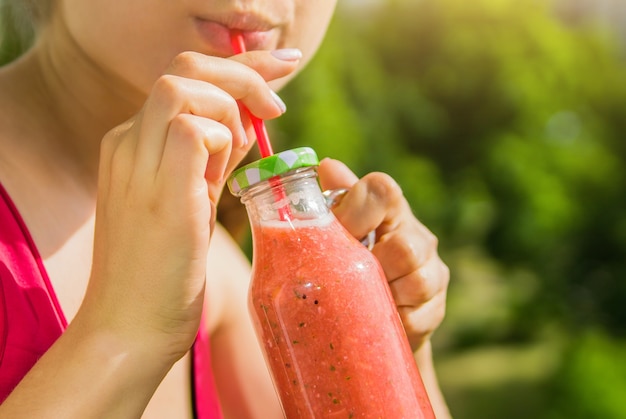 Woman drinks fruity smoothie in glass bottle with straw outside