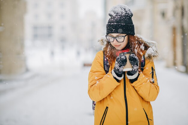 여자는 눈 덮인 겨울 아침 야외에서 아늑한 컵에서 뜨거운 차 또는 커피를 마신다