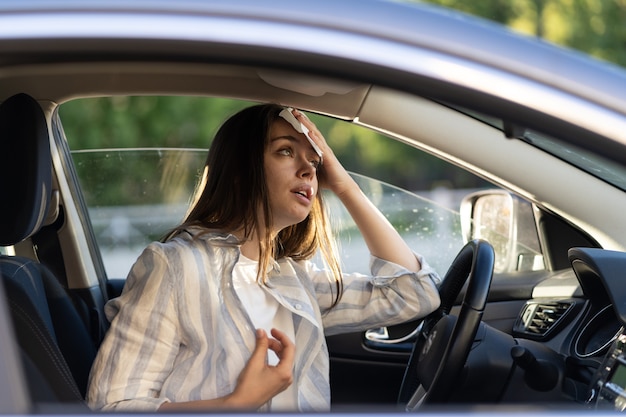 La donna che guida è calda durante l'ondata di caldo in auto che soffre di caldo asciuga il sudore dalla fronte