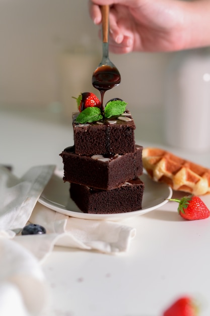 Woman drizzling down chocolate sauce on stack chocolate brownies