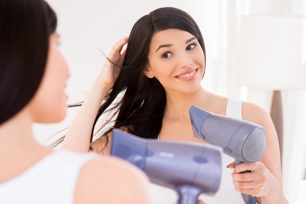 Woman drying hair. Attractive young woman drying her hair while looking at the mirror