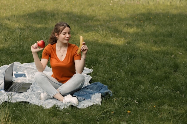여자는 공원에서 사과와 바나나를 먹는다