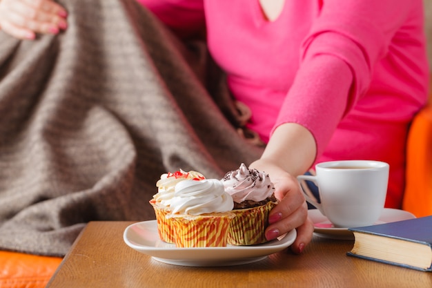 女性はカップケーキを食べ、お茶を飲む