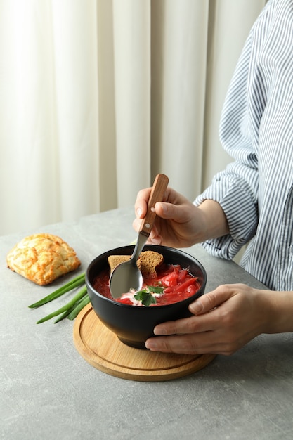 Woman eat tasty borscht on gray table with bread and onion