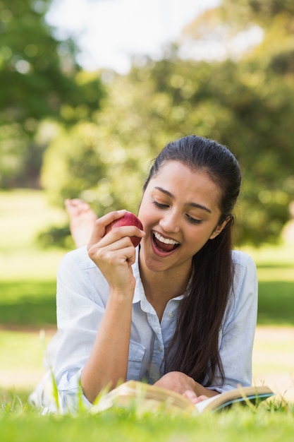 Woman eating apple while reading a book in park