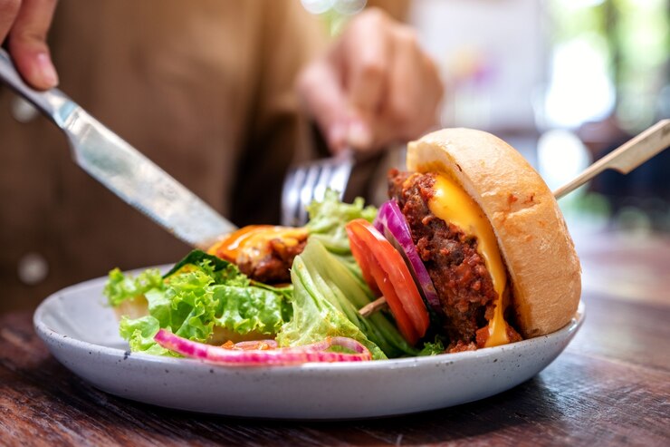 Photo レストランでナイフとフォークでビーフハンバーガーを食べる女性