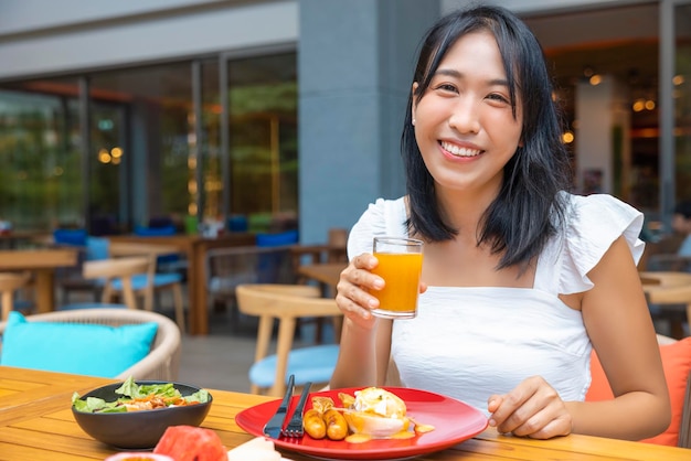 朝食エッグベネディクトフルーツなどスイカパパイヤメロンパッションフルーツオレンジジュースを食べる女性