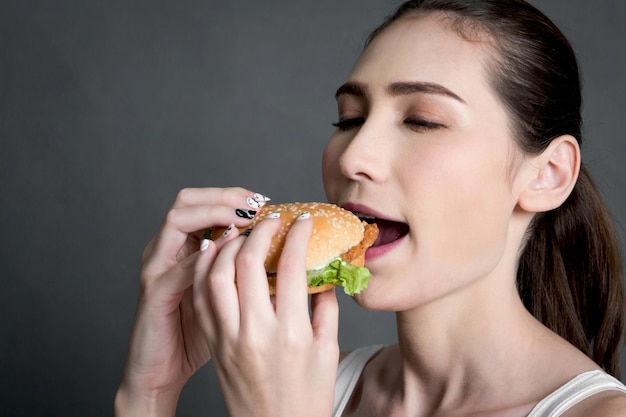 写真 灰色の背景でハンバーガーを食べている女性