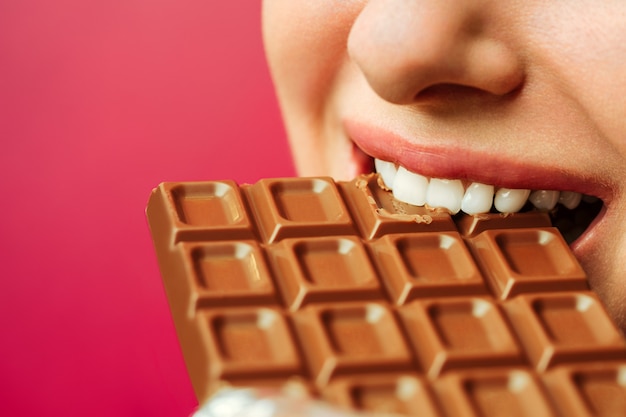 ピンクの背景にチョコレート分離物を食べる女性