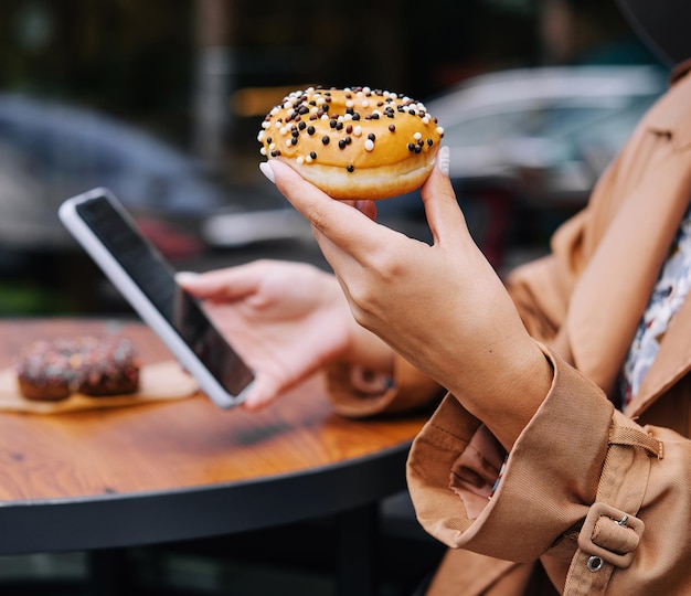 Foto donna che mangia ciambelle e guarda il telefono