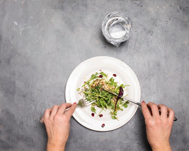 灰色の背景に白い皿に新鮮な緑の芽 microgreens と種子を食べる女性