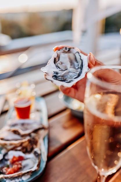 夏の日没時に新鮮な牡蠣を食べ、冷えたプロセッコワインを飲む女性。シーフード料理