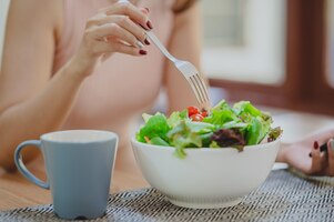 Woman eating fresh vegetable salad in white bowl in kitchen. enjoying a healthy food