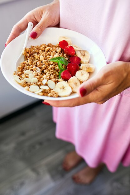 Женщина ест здоровую миску для завтрака, держит в руке мюсли, семена, свежую клубнику, банан, вид сверху, пространство для копирования. чистое питание, детокс, диета, концепция вегетарианской пищи