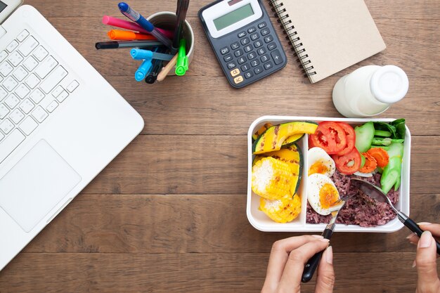 Photo woman eating healthy breakfast in box with rice berry and boiled egg on workspace desk