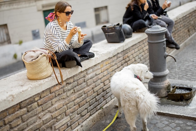 야외 거리에 개와 함께 앉아 아이스크림을 먹는 여자