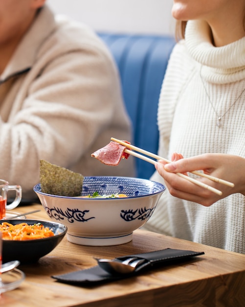 Женщина ест японский суп с лапшой рамэн с палочками для еды
