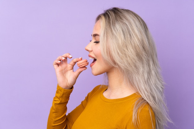 Woman eating macaroons over wall