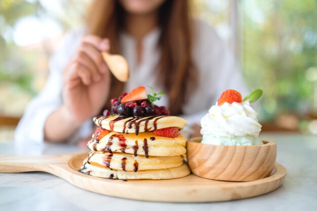 A woman eating a mixed berries pancakes with ice cream and whipped cream by wooden spoon