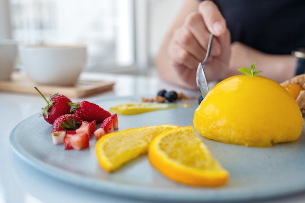 Una donna che mangia torta all'arancia con frutta mista da un cucchiaio nella caffetteria