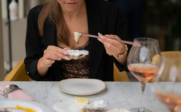 写真 レストランの外のテーブルに座って箸で牡蠣を食べる女性。贅沢の概念