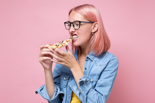 Photo woman eating a piece of pizza against a pink background