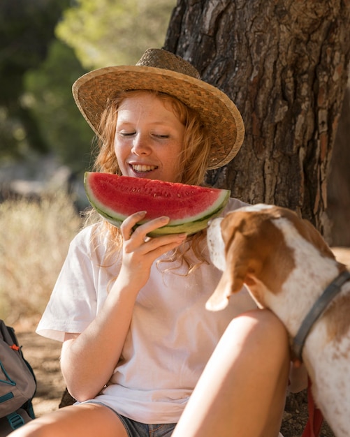 Woman eating a slice of watermelon and dog is looking