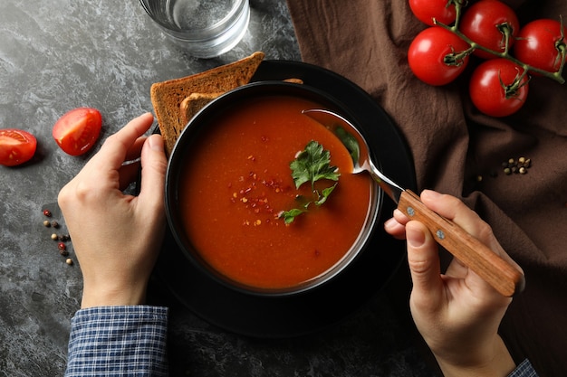 Woman eating tasty tomato soup on dark