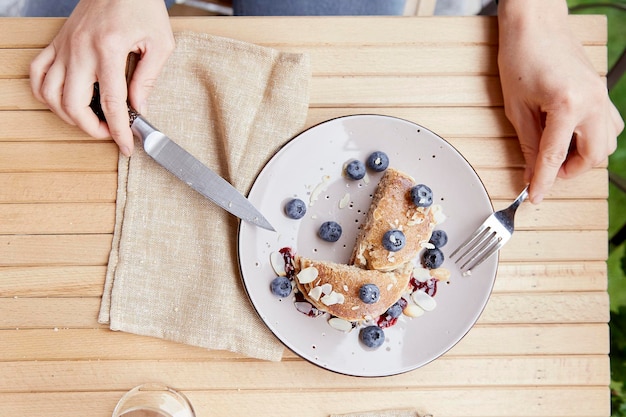 Woman eating traditional pancakes with fresh blueberries and agave syrup on a plate Breakfast outside