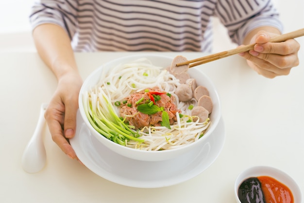 Woman eating traditional Vietnamese Pho noodle using chopsticks.