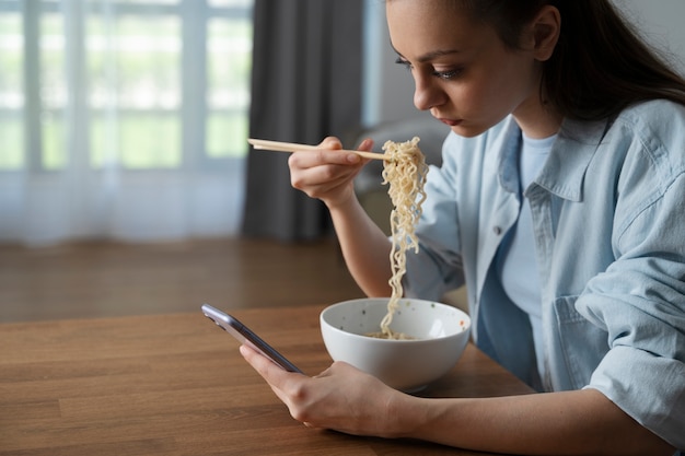 Foto donna che mangia con la vista laterale dello smartphone