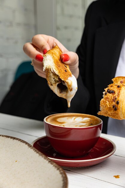 A woman eats a croissant and a cup of coffee.