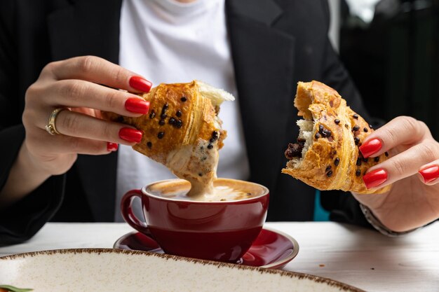 A woman eats a croissant with a cup of coffee.