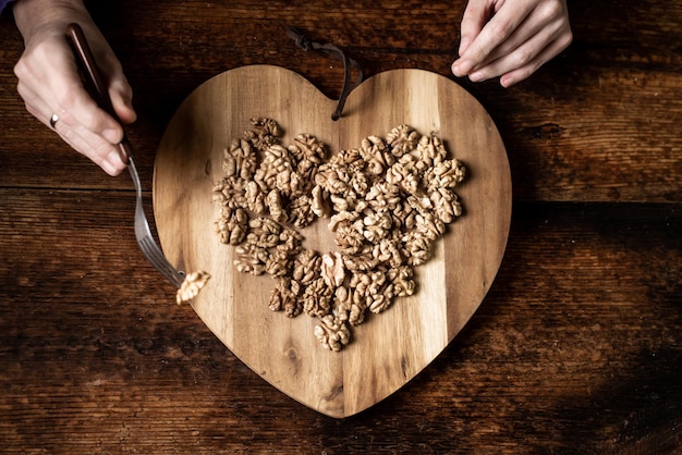 A woman eats nuts from a wooden tray in the shape of a heart Wooden background Shelled walnuts Healthy eating