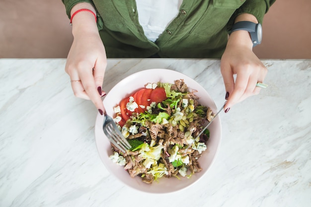 woman eats rich salad with fork and knife. Top view
