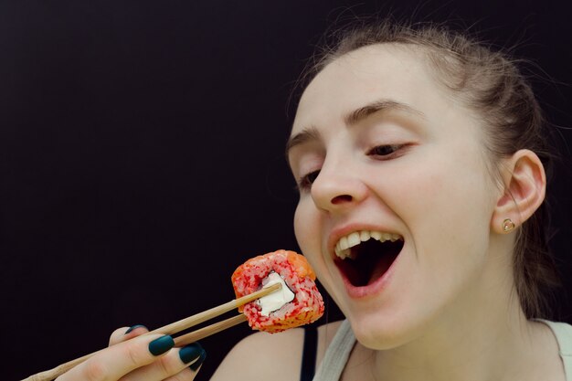 Woman eats rolls with chopsticks. 