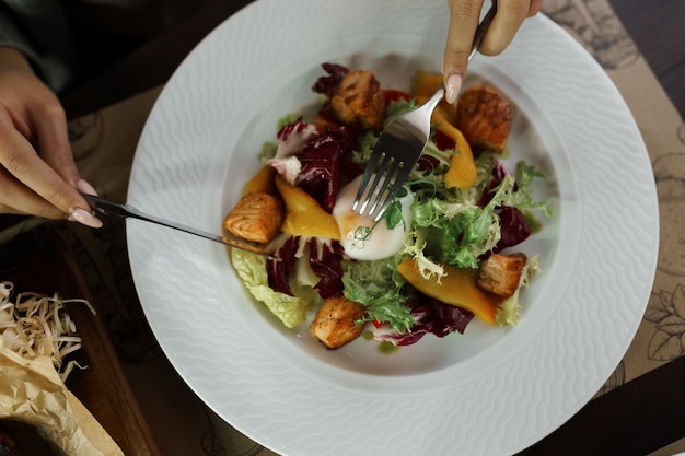 Foto la donna mangia un'insalata di verdure fresche con foglie di insalata verde e peperone giallo fresco con pezzi di pesce e un uovo in camicia in un ristorante. primo piano vista dall'alto. colazione salutare