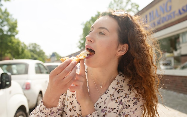 Foto una donna mangia una fetta di pizza in una giornata di sole.