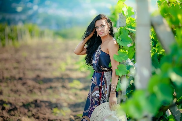 Женщина в элегантной одежде и красивой косметике стоит возле виноградной лозы