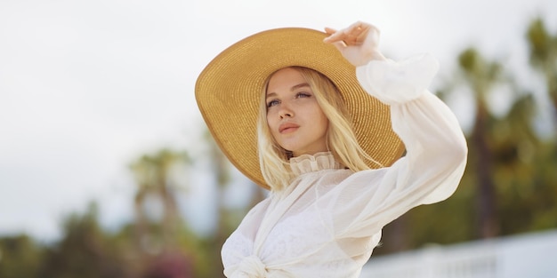 Woman in elegant beach outfit outdoors against palm trees on the background during summer