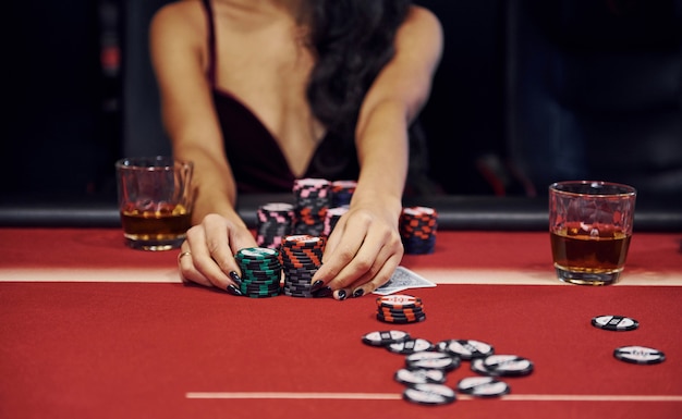 Woman in elegant clothes sits in cassino by table and plays poker game