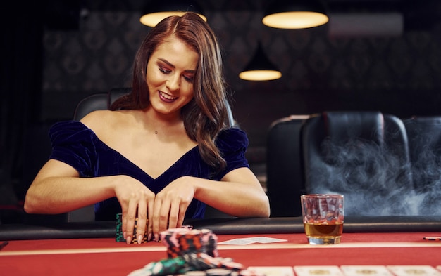 La donna in abiti eleganti si siede in cassino al tavolo e gioca a poker