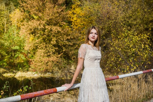 Woman in elegant evening dress posing in autumn park. Sunlights on trees in yellow colours