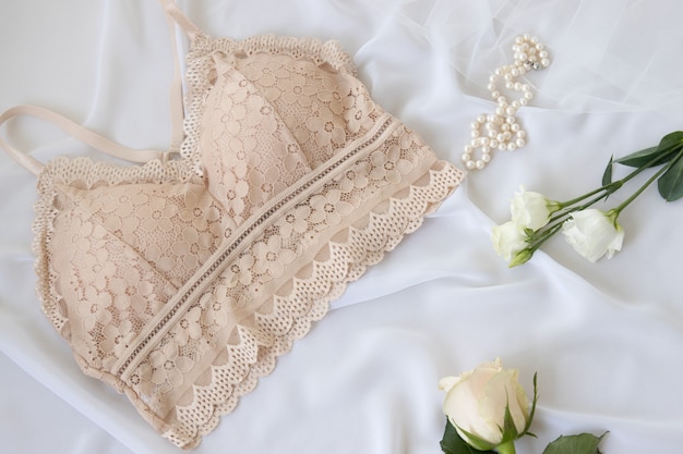 Reggiseno di pizzo nudo elegante donna fiori, gioielli, profumo su sfondo bianco. disposizione piana della biancheria alla moda. concetto di moda intimo