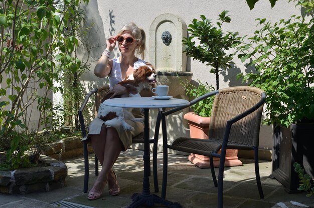 Foto donna in eleganti abiti estivi con il cane - cavalier king charles spaniel - nelle ombre del giardino