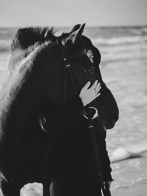 Foto donna che abbraccia un cavallo mentre è in piedi sulla riva della spiaggia