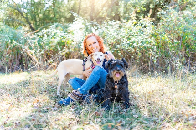 Woman embracing two dogs sitting in a field